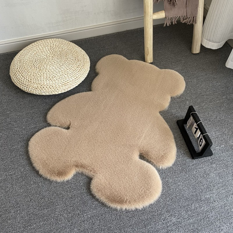 Beige teddy bear-shaped rug on a gray floor with a woven mat and chair in the background.