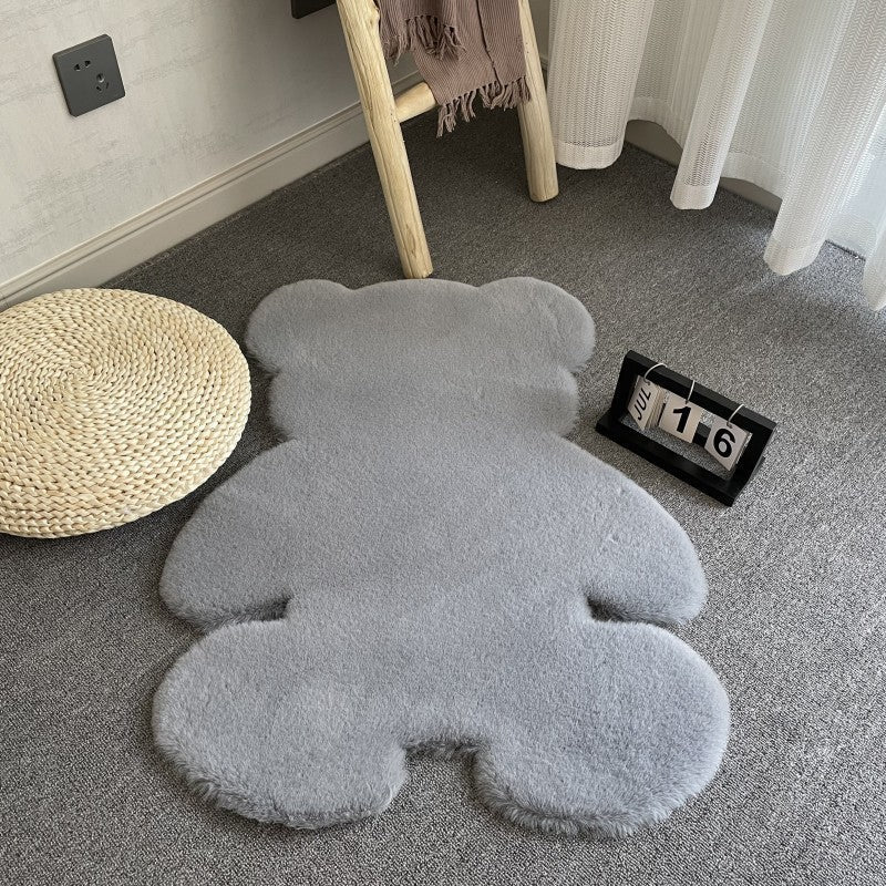 Gray teddy bear-shaped rug on a carpeted floor with a chair and round pillow in the background.